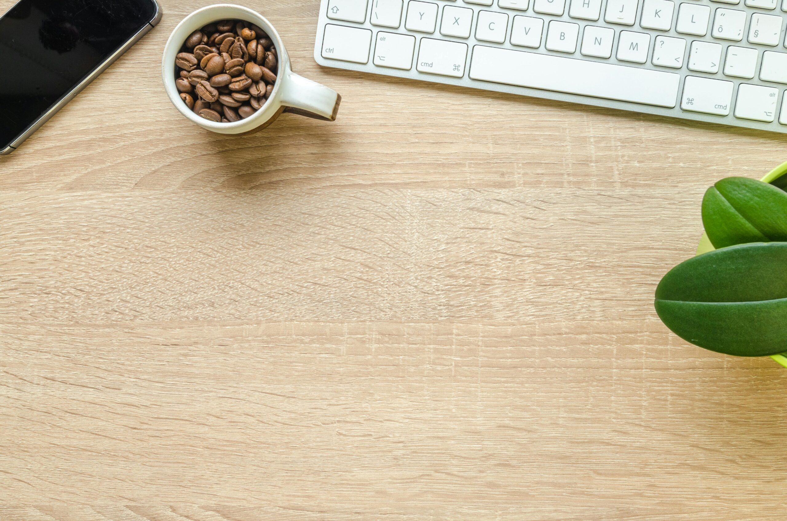 Flat lay of a clean desk with coffee beans, plant, smartphone, and keyboard.